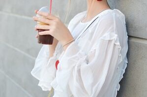 woman leaning on wall holding cups of black beverage
