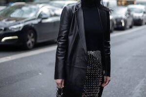 woman in black leather jacket standing on sidewalk during daytime