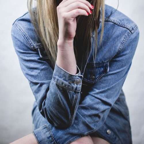 woman in blue denim jacket wearing red sunglasses and red manicure with hands on chin