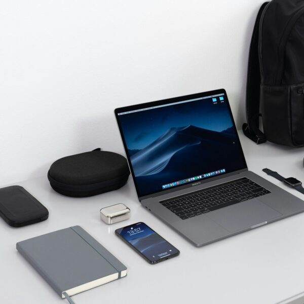 MacBook Pro on table near black smartphone, cordless headphones and backpack